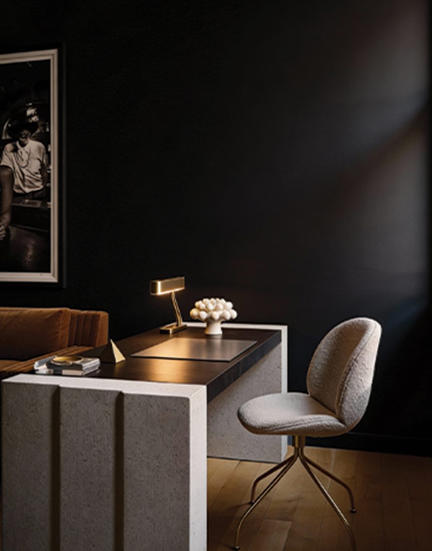 Executive desk with a brass lamp and boucle chair against a dark wall